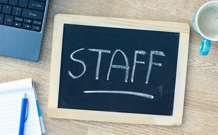 A chalkboard saying staff with office items on a desk